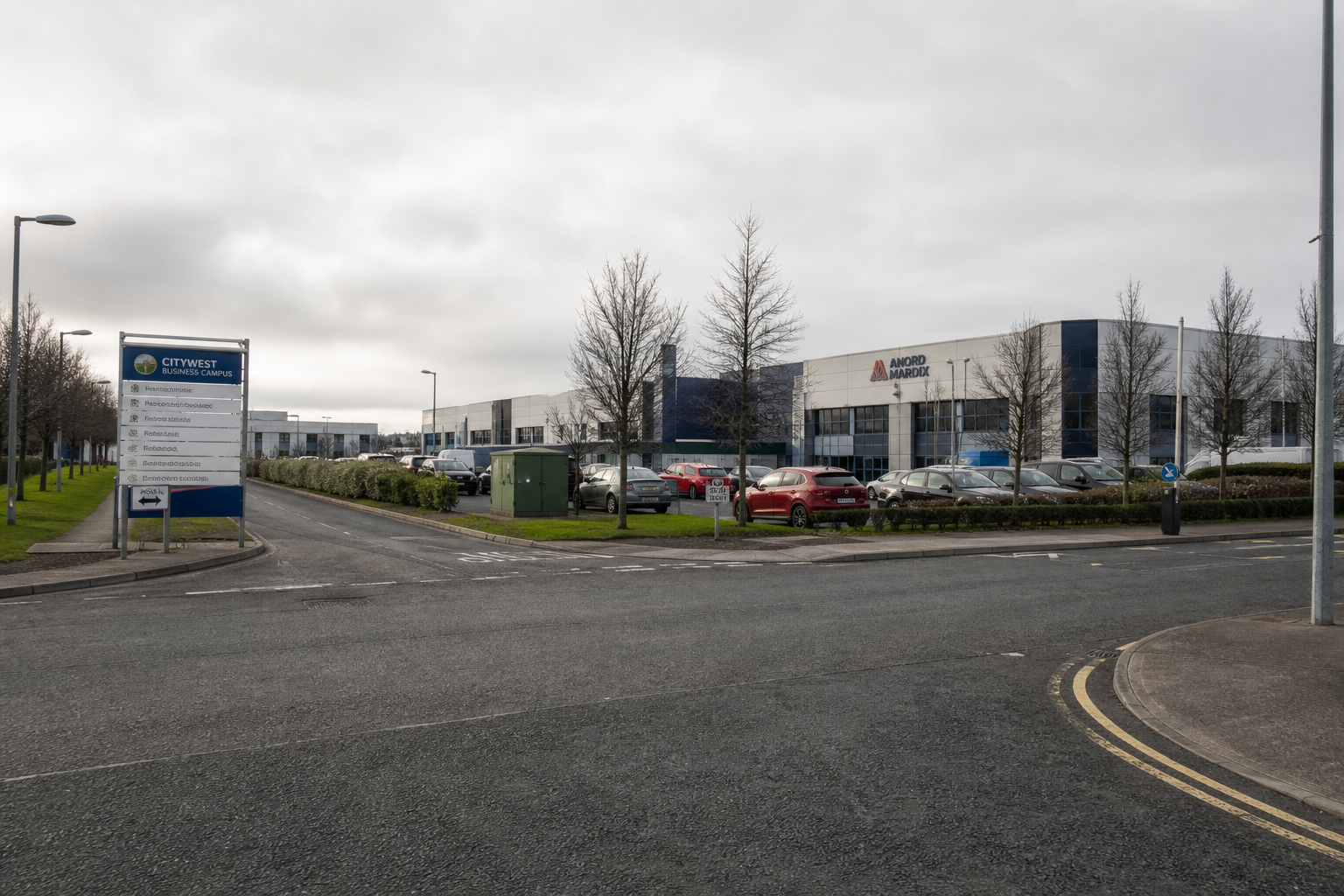 Citywest business park — low-rise warehouses with loading docks, M50 overpass in the background, hi-vis worker walking between units